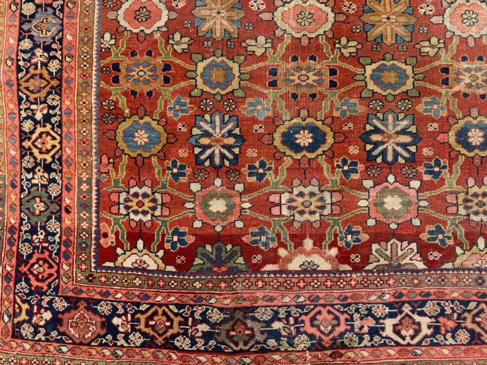 An antique Sultanabad hand-knotted wool carpet featuring an all-over repeating geometric floral pattern on a terracotta red field with a dark blue patterned border. View X