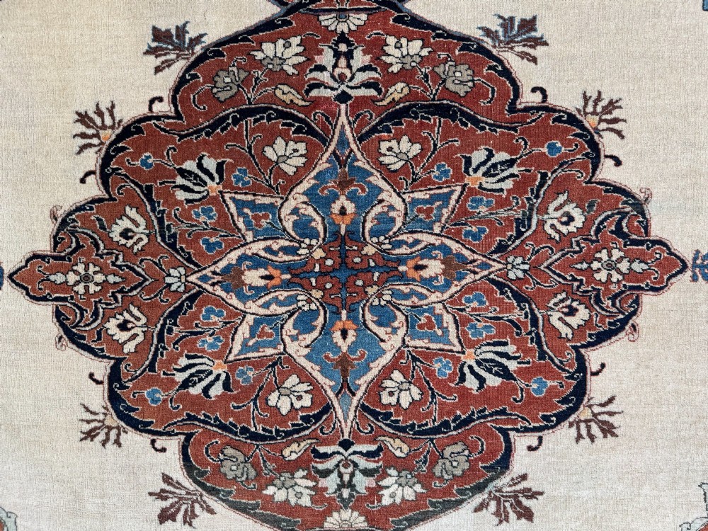 An antique Persian Tabriz wool carpet featuring a complex terracotta and navy central medallion on an ivory field with layered floral borders. View IV