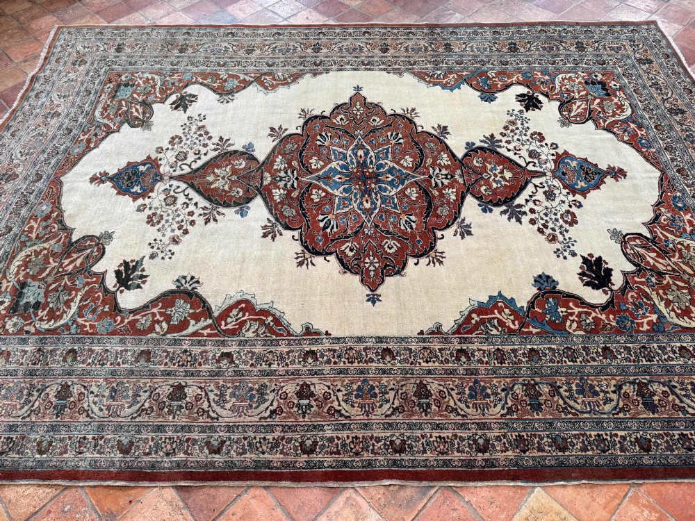 An antique Persian Tabriz wool carpet featuring a complex terracotta and navy central medallion on an ivory field with layered floral borders. View VIII