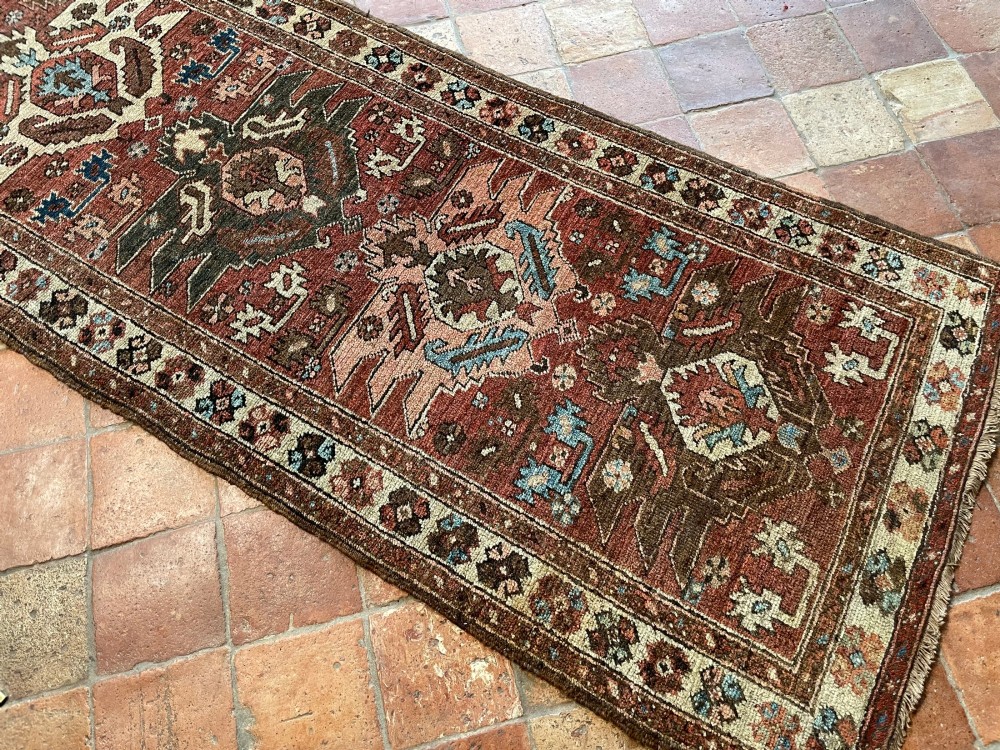 An antique Bakshaish hand-knotted wool runner rug featuring geometric tribal medallions in terracotta red, indigo blue, cream, and brown along a long narrow field with decorative borders. View II
