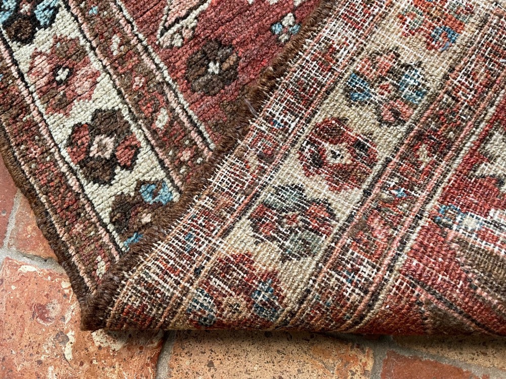 An antique Bakshaish hand-knotted wool runner rug featuring geometric tribal medallions in terracotta red, indigo blue, cream, and brown along a long narrow field with decorative borders. View III