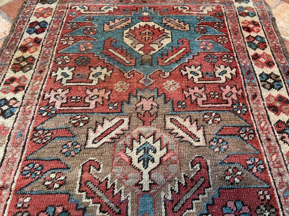 An antique Bakshaish hand-knotted wool runner rug featuring geometric tribal medallions in terracotta red, indigo blue, cream, and brown along a long narrow field with decorative borders. View IV