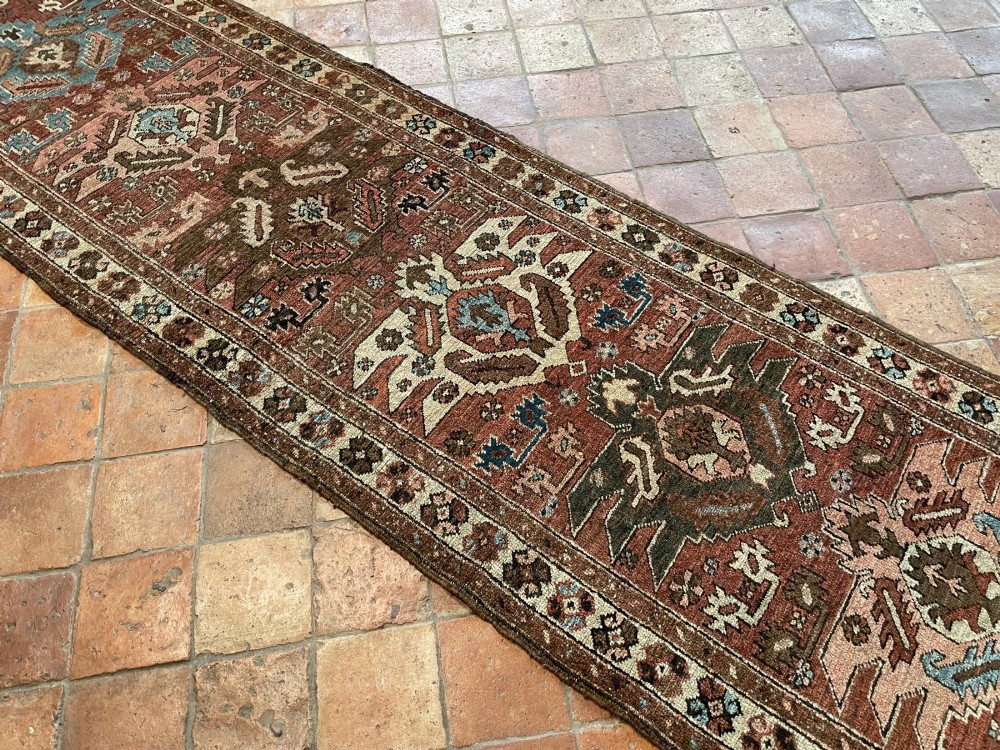 An antique Bakshaish hand-knotted wool runner rug featuring geometric tribal medallions in terracotta red, indigo blue, cream, and brown along a long narrow field with decorative borders. View V