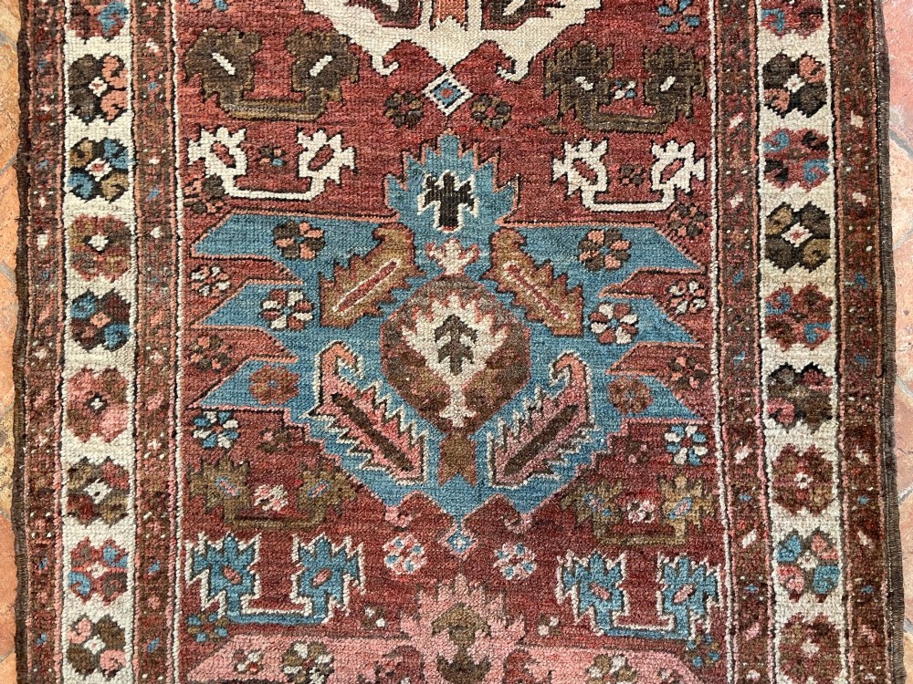 An antique Bakshaish hand-knotted wool runner rug featuring geometric tribal medallions in terracotta red, indigo blue, cream, and brown along a long narrow field with decorative borders. View VI
