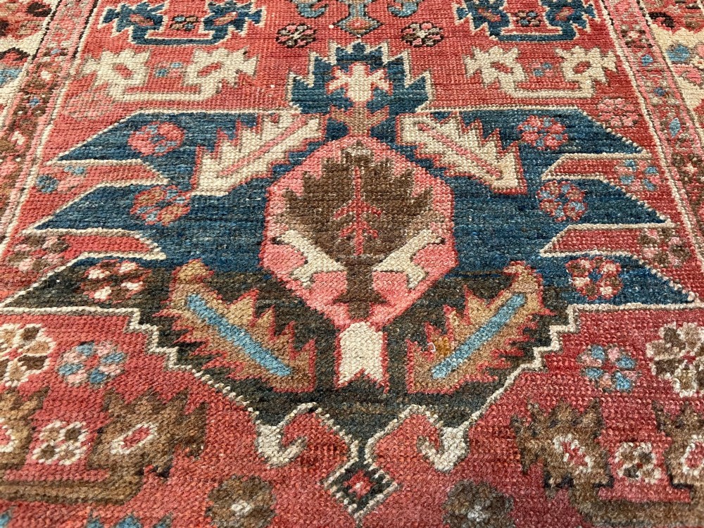 An antique Bakshaish hand-knotted wool runner rug featuring geometric tribal medallions in terracotta red, indigo blue, cream, and brown along a long narrow field with decorative borders. View VII