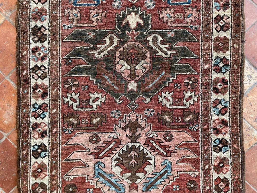 An antique Bakshaish hand-knotted wool runner rug featuring geometric tribal medallions in terracotta red, indigo blue, cream, and brown along a long narrow field with decorative borders. View IX
