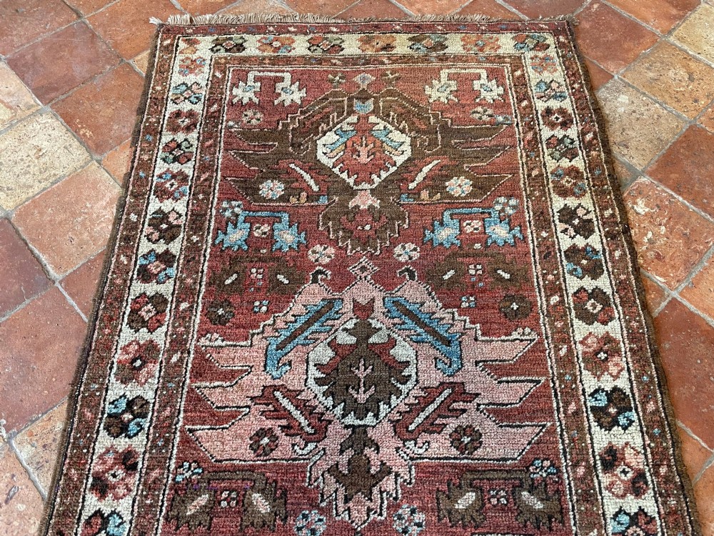 An antique Bakshaish hand-knotted wool runner rug featuring geometric tribal medallions in terracotta red, indigo blue, cream, and brown along a long narrow field with decorative borders. View X