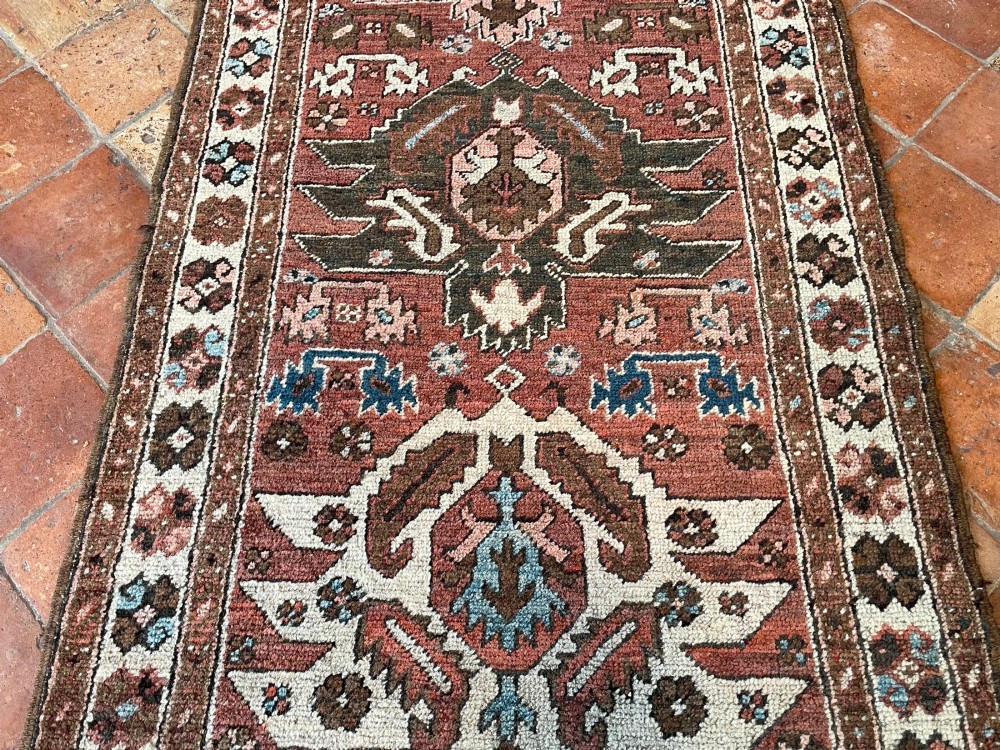 An antique Bakshaish hand-knotted wool runner rug featuring geometric tribal medallions in terracotta red, indigo blue, cream, and brown along a long narrow field with decorative borders. View XI
