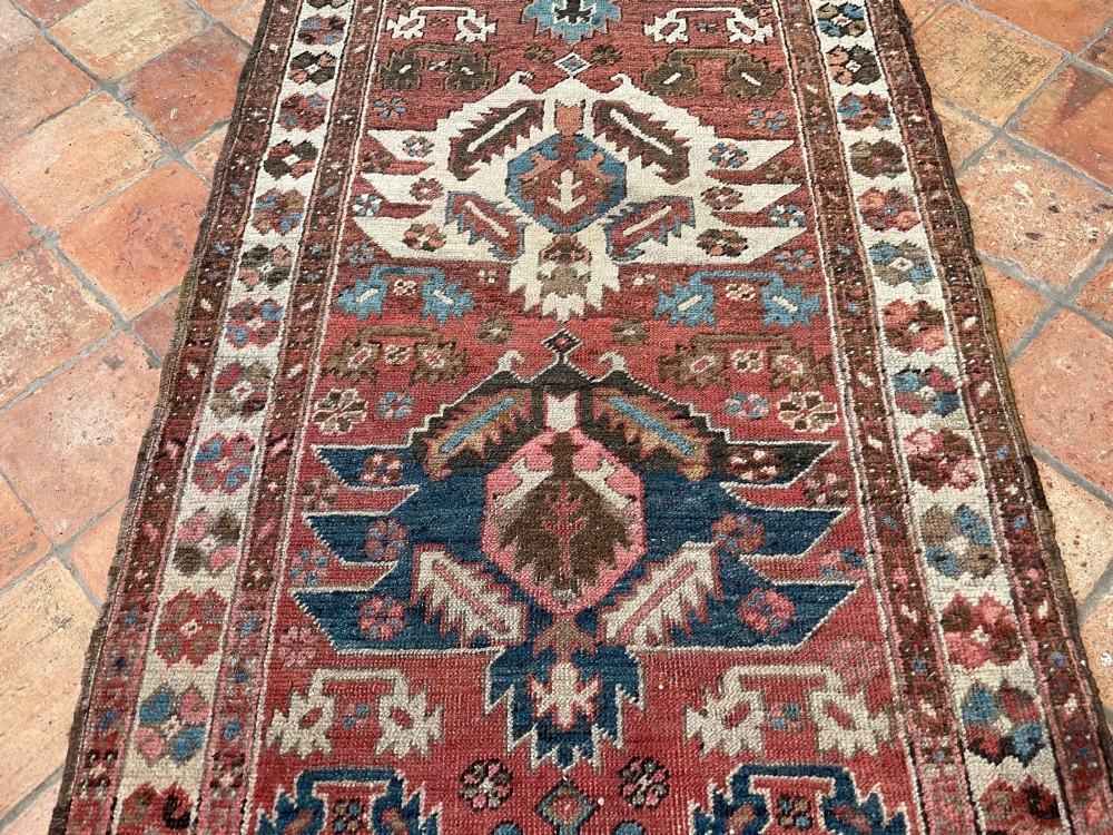 An antique Bakshaish hand-knotted wool runner rug featuring geometric tribal medallions in terracotta red, indigo blue, cream, and brown along a long narrow field with decorative borders. View XII