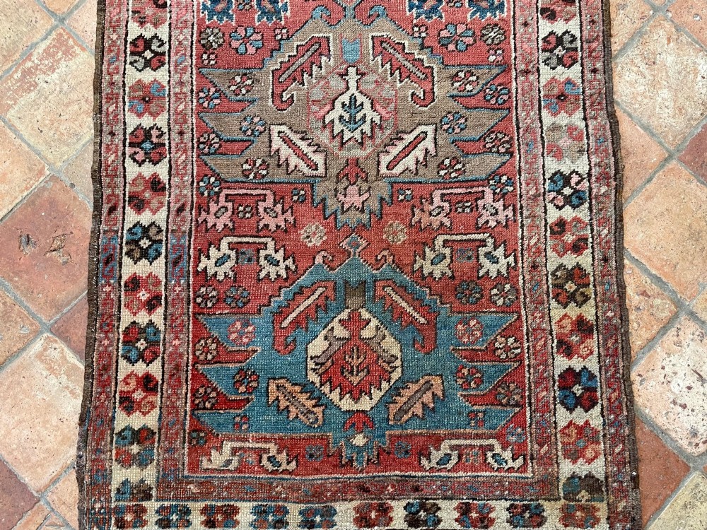 An antique Bakshaish hand-knotted wool runner rug featuring geometric tribal medallions in terracotta red, indigo blue, cream, and brown along a long narrow field with decorative borders. View XIII
