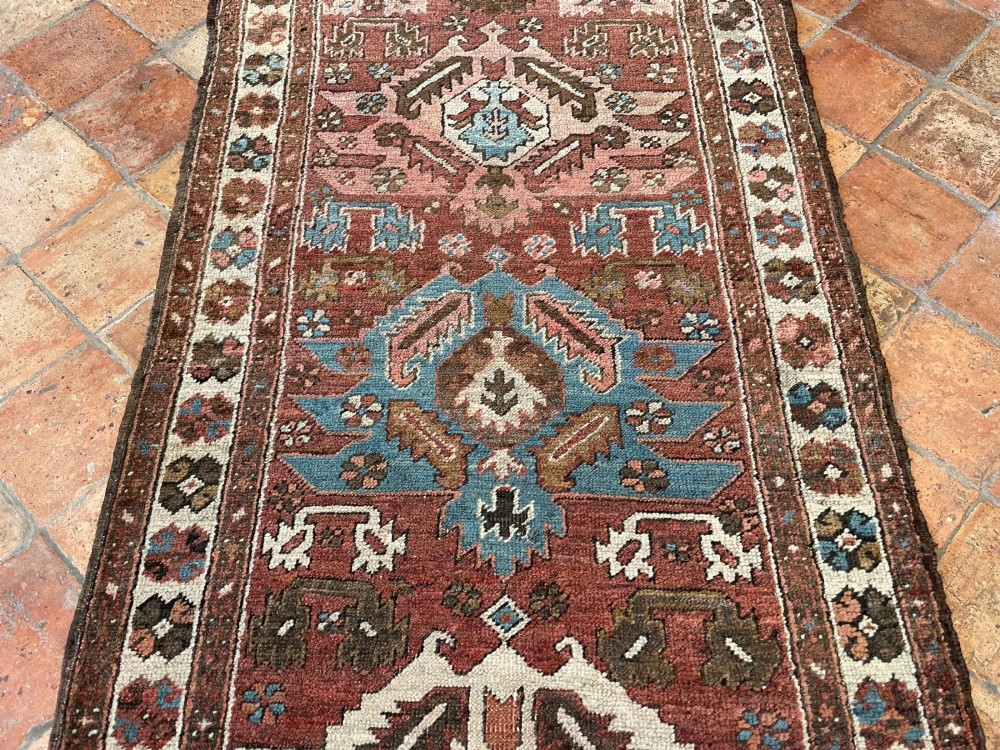 An antique Bakshaish hand-knotted wool runner rug featuring geometric tribal medallions in terracotta red, indigo blue, cream, and brown along a long narrow field with decorative borders. View XIV