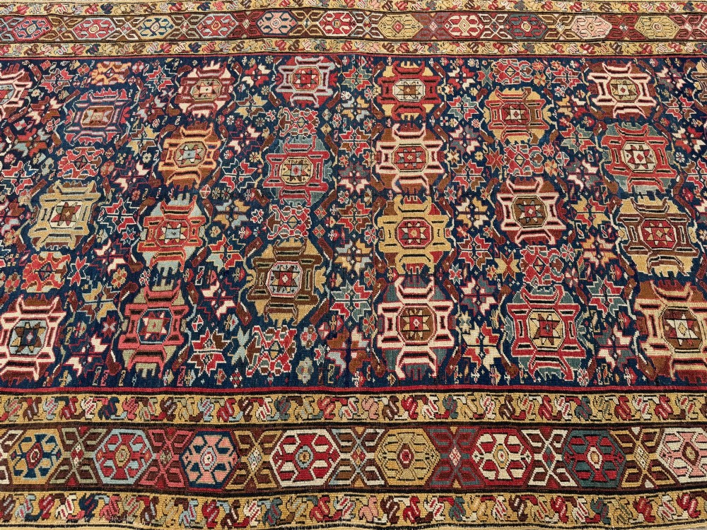 An elongated antique hand-knotted Caucasian Kuba Kelleh rug with a navy blue field featuring geometric repeating medallions framed by patterned multicoloured borders. View II