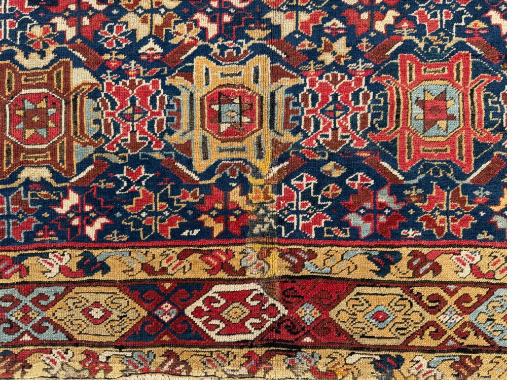 An elongated antique hand-knotted Caucasian Kuba Kelleh rug with a navy blue field featuring geometric repeating medallions framed by patterned multicoloured borders. View III