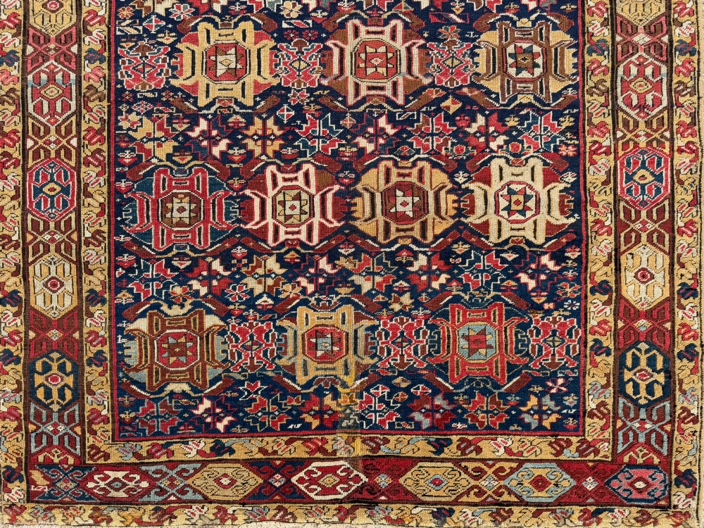 An elongated antique hand-knotted Caucasian Kuba Kelleh rug with a navy blue field featuring geometric repeating medallions framed by patterned multicoloured borders. View IV