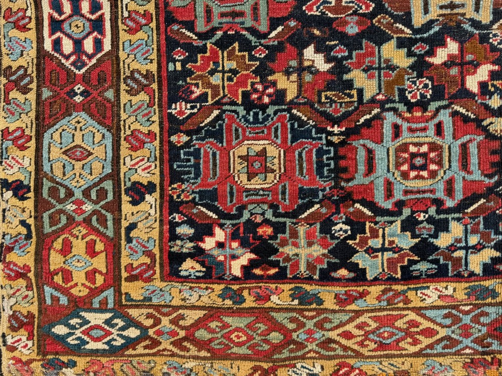 An elongated antique hand-knotted Caucasian Kuba Kelleh rug with a navy blue field featuring geometric repeating medallions framed by patterned multicoloured borders. View VI