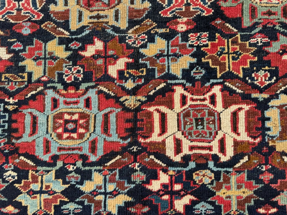 An elongated antique hand-knotted Caucasian Kuba Kelleh rug with a navy blue field featuring geometric repeating medallions framed by patterned multicoloured borders. View VII