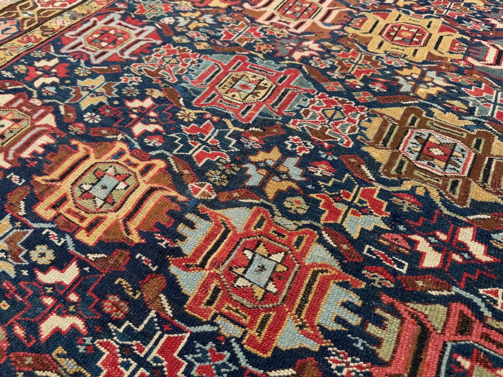 An elongated antique hand-knotted Caucasian Kuba Kelleh rug with a navy blue field featuring geometric repeating medallions framed by patterned multicoloured borders. View IX