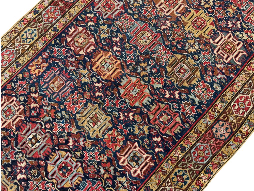 An elongated antique hand-knotted Caucasian Kuba Kelleh rug with a navy blue field featuring geometric repeating medallions framed by patterned multicoloured borders. View X