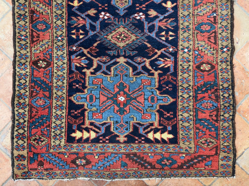 An antique Karaja hand-knotted wool runner featuring geometric blue and terracotta medallions on a dark navy field.