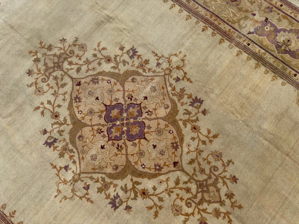 An antique hand-knotted rectangular wool carpet featuring a light cream field, a central floral medallion, corner spandrels, and a patterned border in shades of purple and ochre. View III