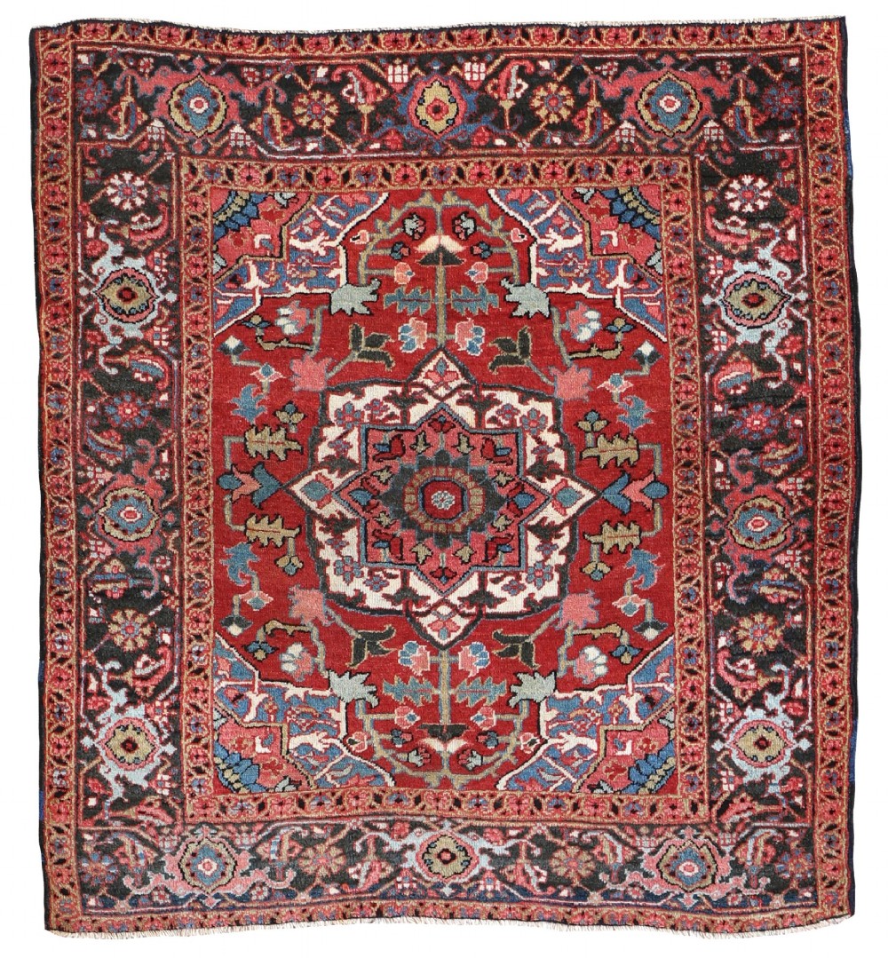 A hand-knotted Persian Heriz rug featuring a central geometric star medallion on a terracotta red field surrounded by an intricate navy blue border.