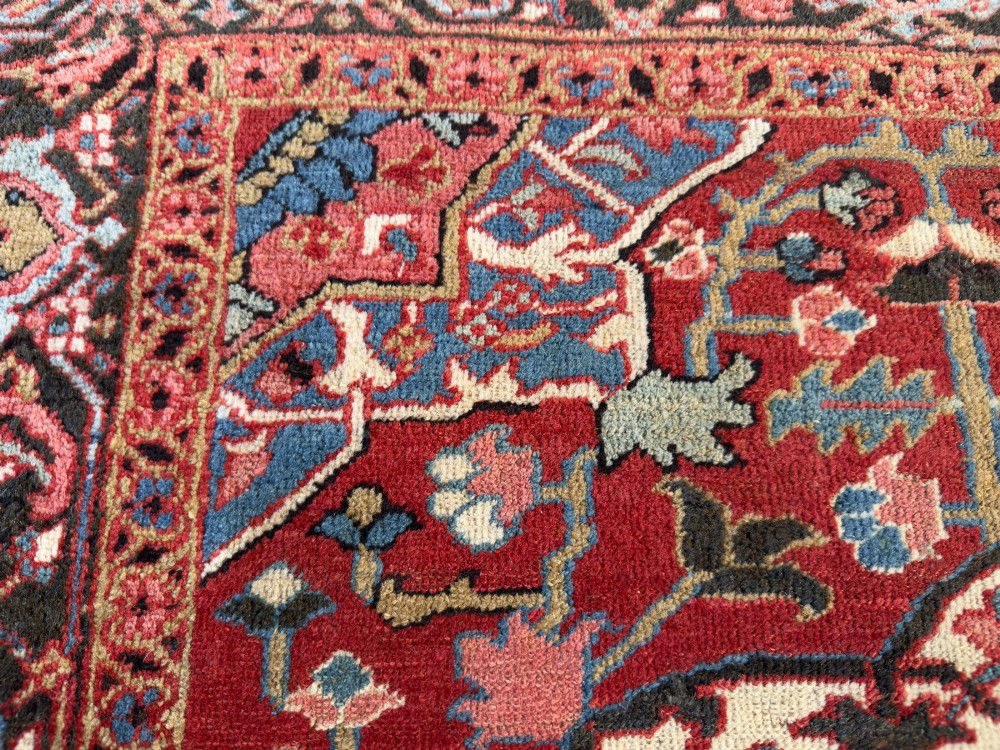 A hand-knotted Persian Heriz rug featuring a central geometric star medallion on a terracotta red field surrounded by an intricate navy blue border. View II