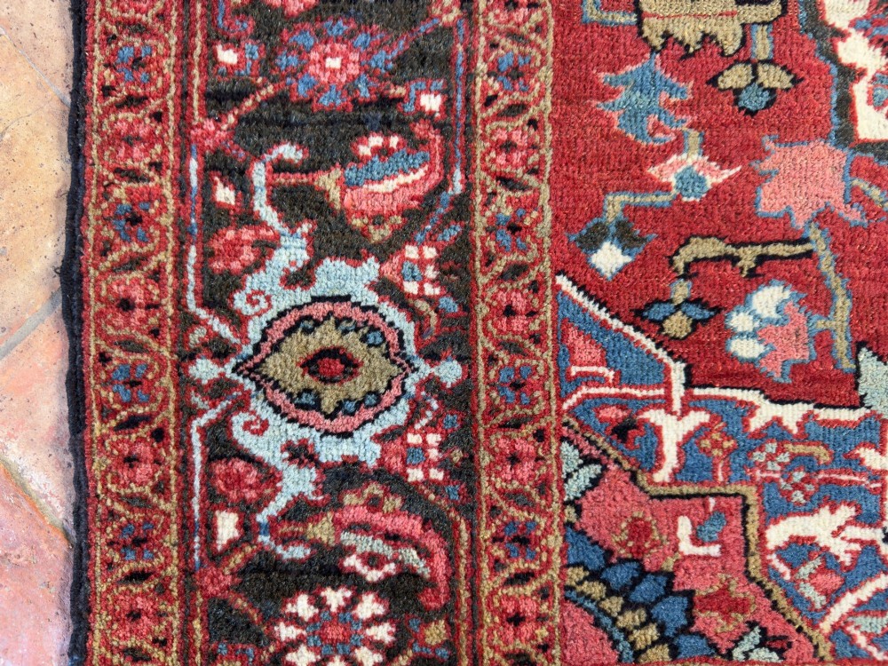 A hand-knotted Persian Heriz rug featuring a central geometric star medallion on a terracotta red field surrounded by an intricate navy blue border. View III