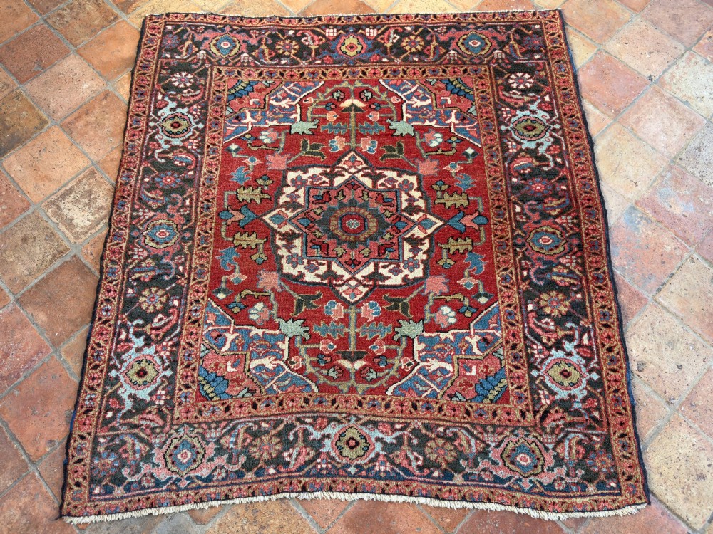 A hand-knotted Persian Heriz rug featuring a central geometric star medallion on a terracotta red field surrounded by an intricate navy blue border. View IV