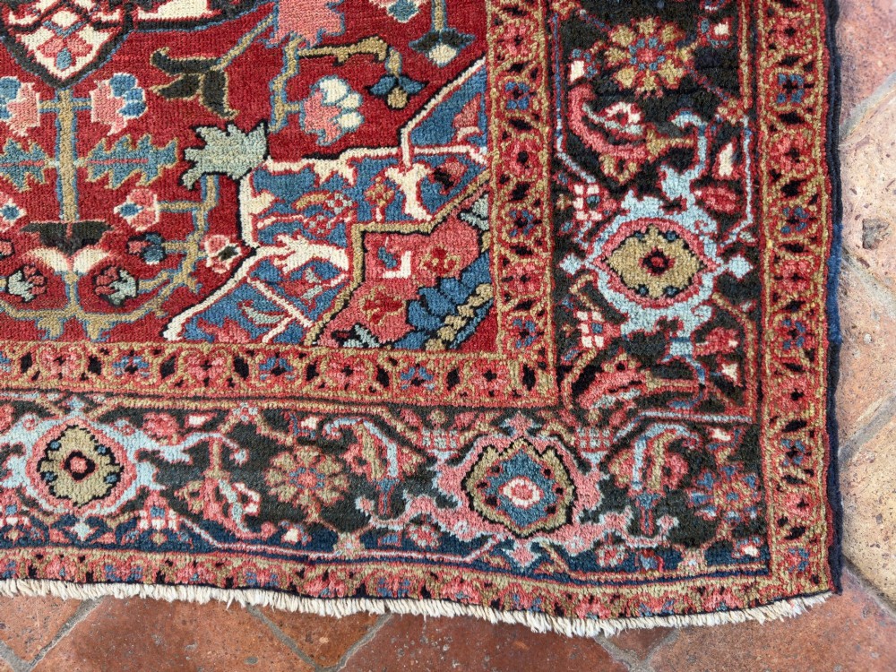 A hand-knotted Persian Heriz rug featuring a central geometric star medallion on a terracotta red field surrounded by an intricate navy blue border. View V