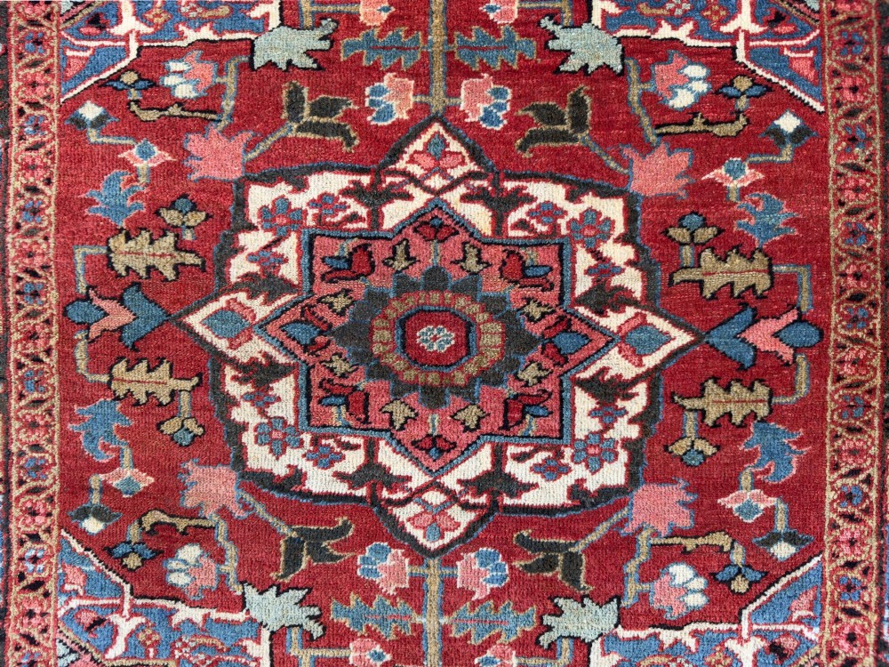 A hand-knotted Persian Heriz rug featuring a central geometric star medallion on a terracotta red field surrounded by an intricate navy blue border. View VI
