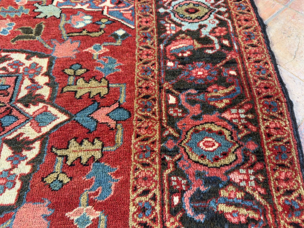 A hand-knotted Persian Heriz rug featuring a central geometric star medallion on a terracotta red field surrounded by an intricate navy blue border. View VII