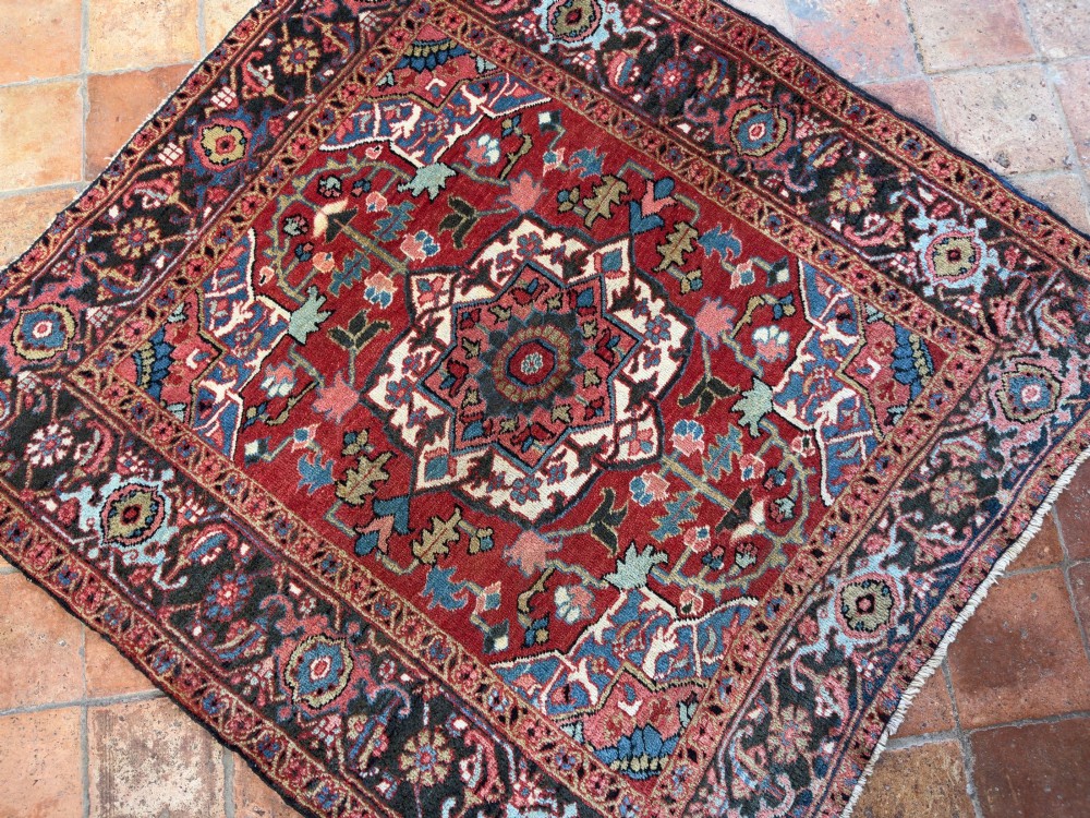 A hand-knotted Persian Heriz rug featuring a central geometric star medallion on a terracotta red field surrounded by an intricate navy blue border. View VIII
