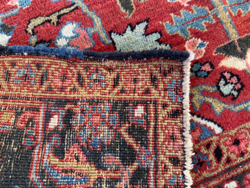 A hand-knotted Persian Heriz rug featuring a central geometric star medallion on a terracotta red field surrounded by an intricate navy blue border. View IX
