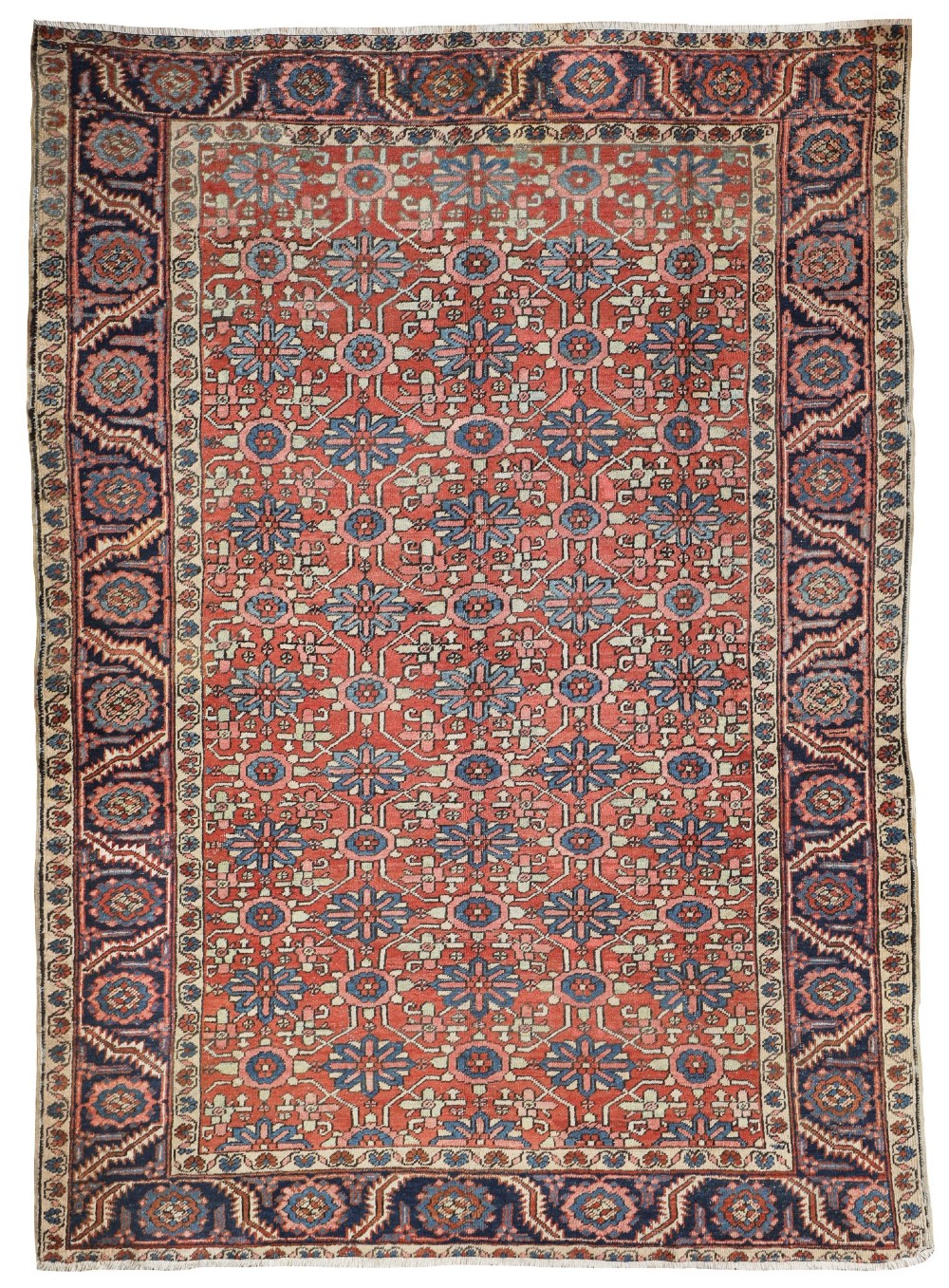 A hand-knotted antique Heriz wool carpet featuring a repeating geometric star motif on a terracotta red field framed by a wide navy blue patterned border.