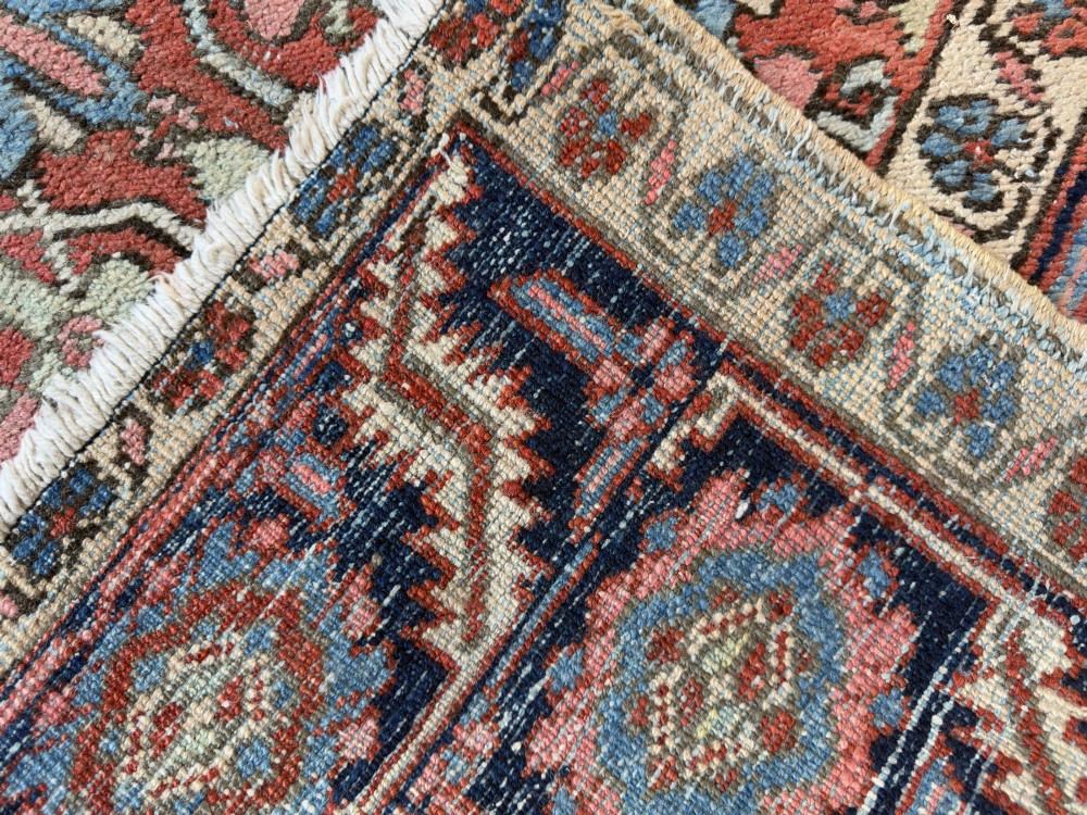 A hand-knotted antique Heriz wool carpet featuring a repeating geometric star motif on a terracotta red field framed by a wide navy blue patterned border. View II