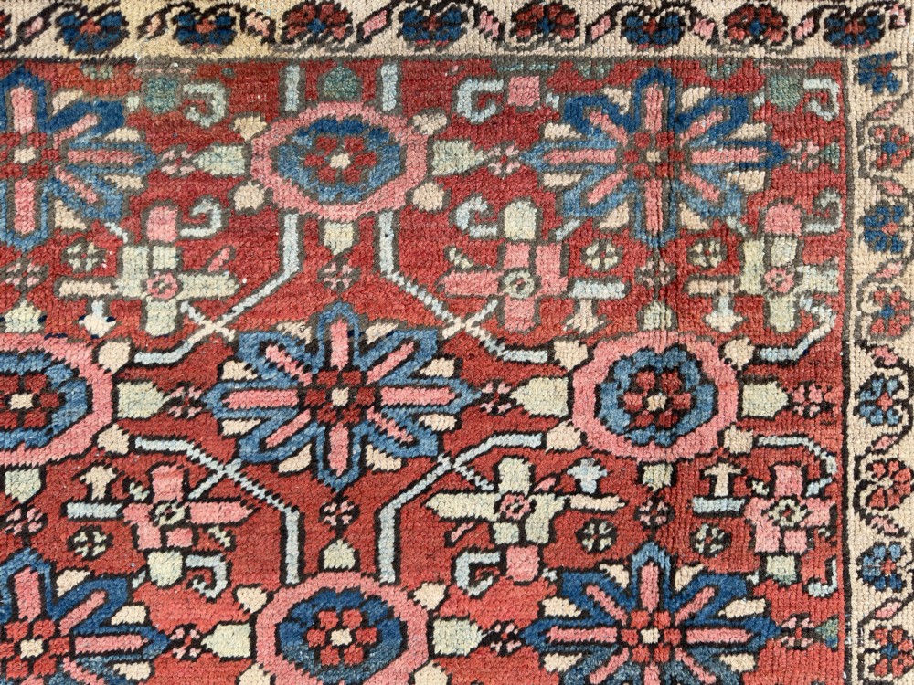 A hand-knotted antique Heriz wool carpet featuring a repeating geometric star motif on a terracotta red field framed by a wide navy blue patterned border. View IX