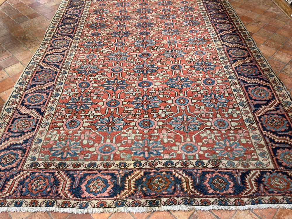 A hand-knotted antique Heriz wool carpet featuring a repeating geometric star motif on a terracotta red field framed by a wide navy blue patterned border. View XIII