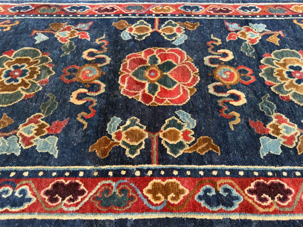An antique hand-knotted Tibetan Khaden rug featuring a deep blue field adorned with three stylised lotus blossoms and red decorative borders. View II