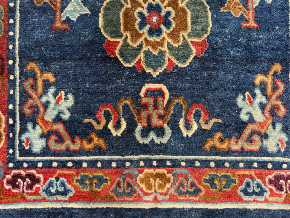 An antique hand-knotted Tibetan Khaden rug featuring a deep blue field adorned with three stylised lotus blossoms and red decorative borders. View V