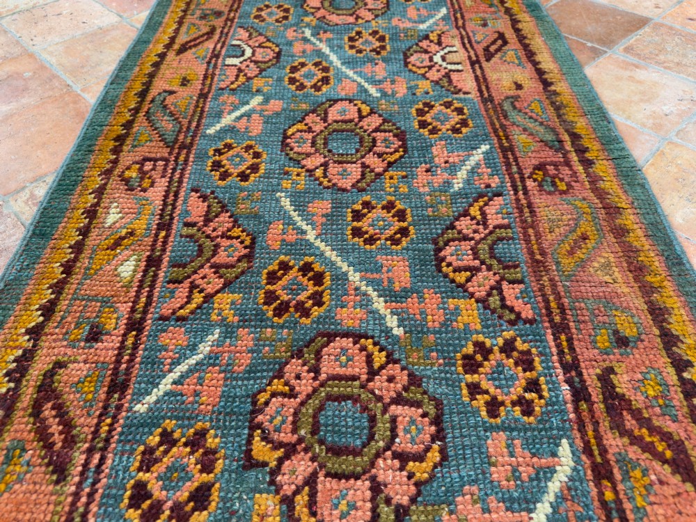 An exceptionally long antique Ushak runner rug displaying a central slate blue panel with repeating coral floral rosettes framed by a wide terracotta patterned border. View II
