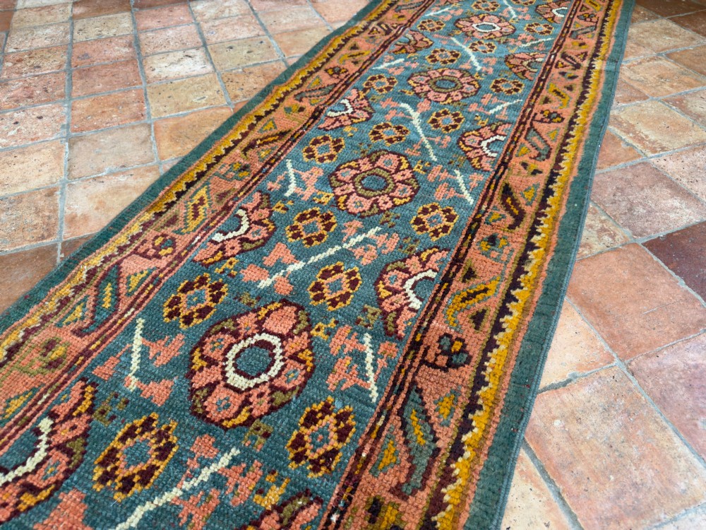 An exceptionally long antique Ushak runner rug displaying a central slate blue panel with repeating coral floral rosettes framed by a wide terracotta patterned border. View IV