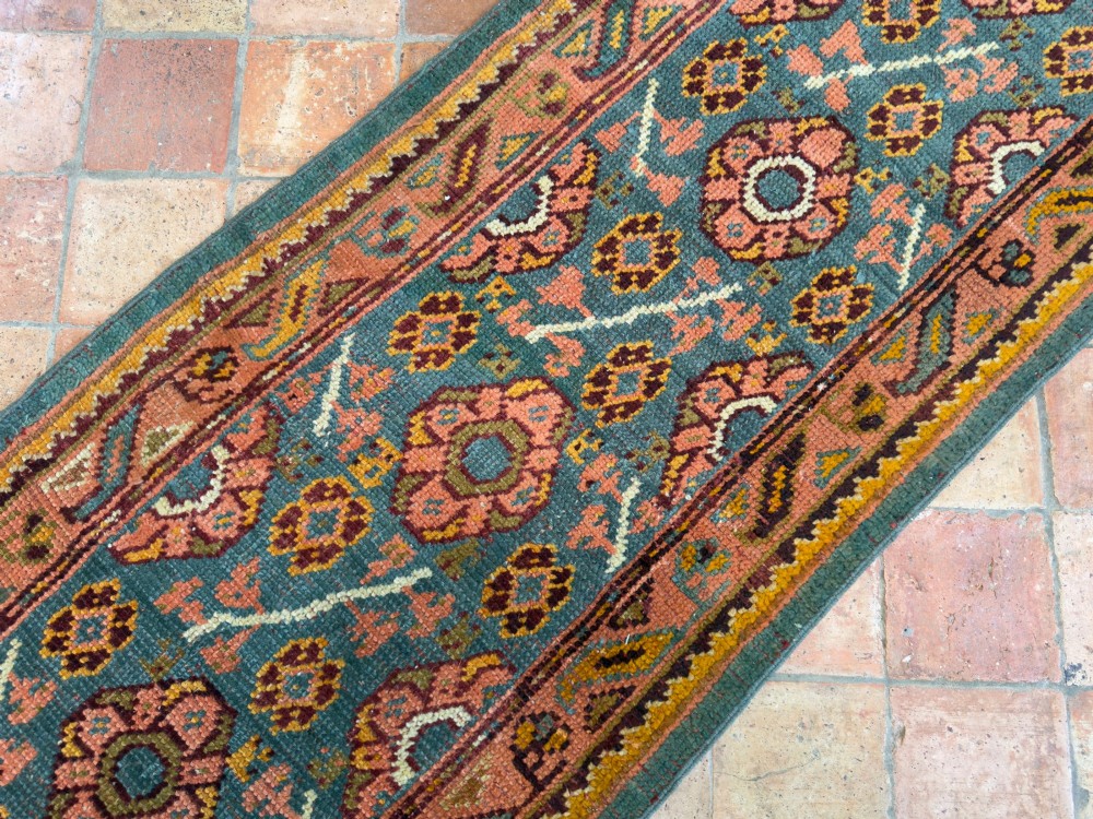 An exceptionally long antique Ushak runner rug displaying a central slate blue panel with repeating coral floral rosettes framed by a wide terracotta patterned border. View V