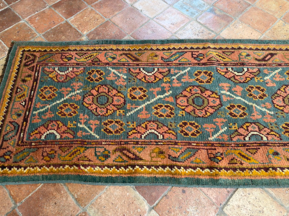 An exceptionally long antique Ushak runner rug displaying a central slate blue panel with repeating coral floral rosettes framed by a wide terracotta patterned border. View VI