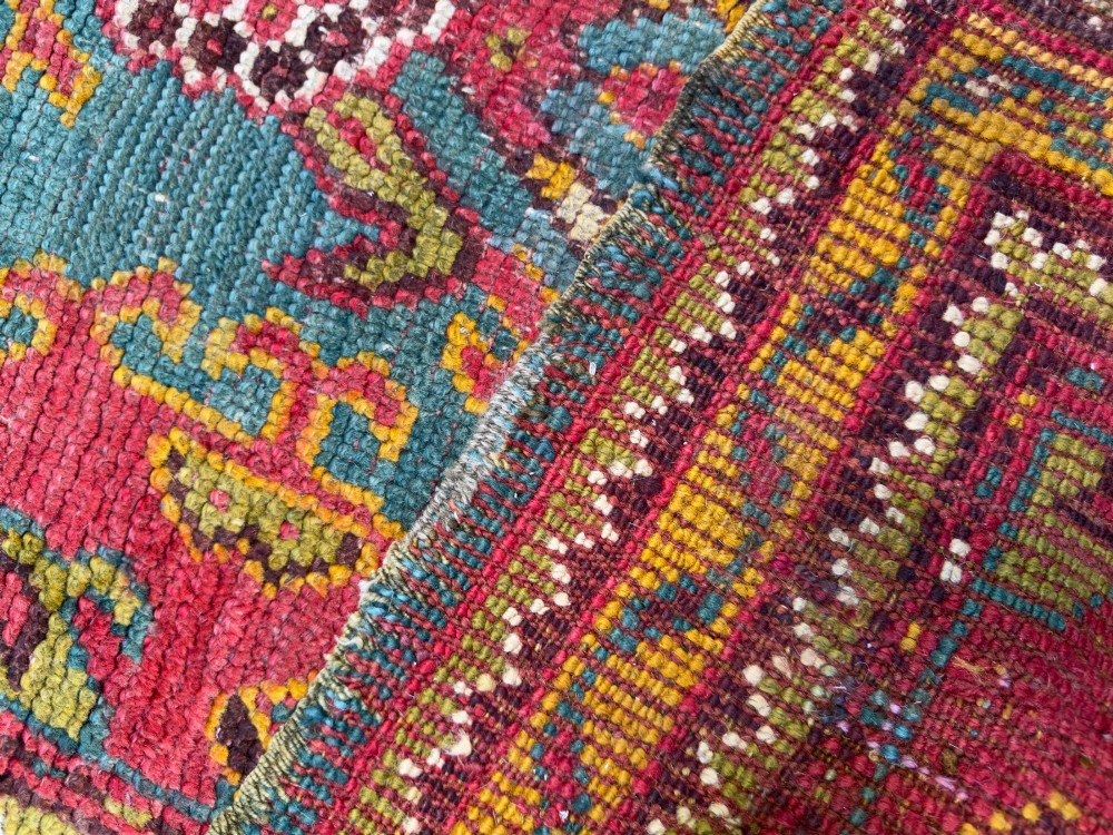 An antique hand-knotted wool runner rug featuring geometric tribal medallions in red, yellow, and orange on a vibrant teal background. View VII