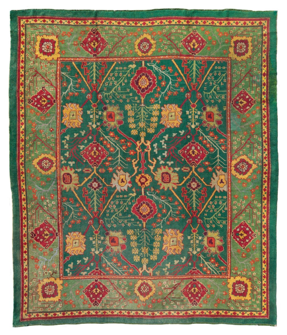 An antique Arts and Crafts hand-knotted wool Donegal carpet featuring a green field filled with stylised red and yellow floral motifs and a decorative geometric border.