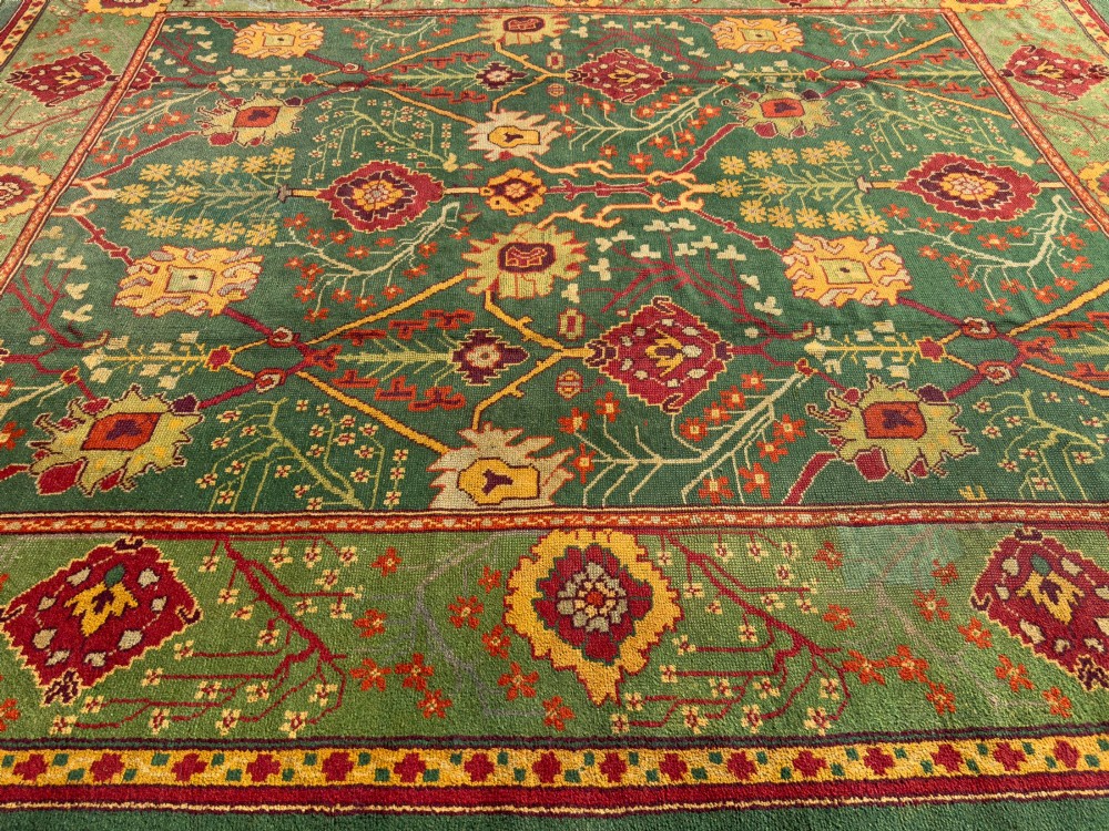 An antique Arts and Crafts hand-knotted wool Donegal carpet featuring a green field filled with stylised red and yellow floral motifs and a decorative geometric border. View II