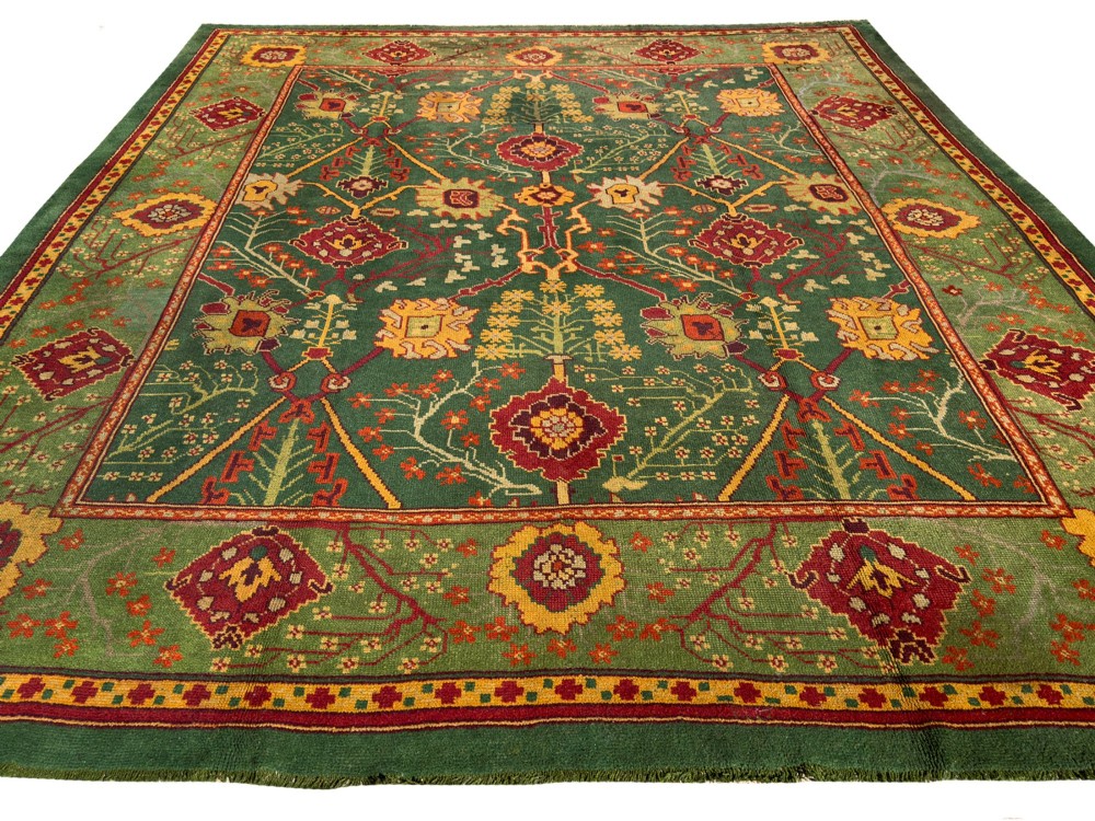 An antique Arts and Crafts hand-knotted wool Donegal carpet featuring a green field filled with stylised red and yellow floral motifs and a decorative geometric border. View III