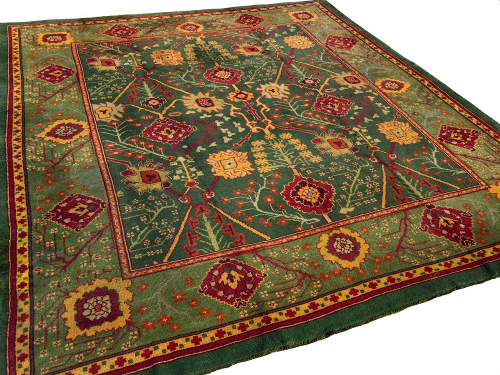 An antique Arts and Crafts hand-knotted wool Donegal carpet featuring a green field filled with stylised red and yellow floral motifs and a decorative geometric border. View IV