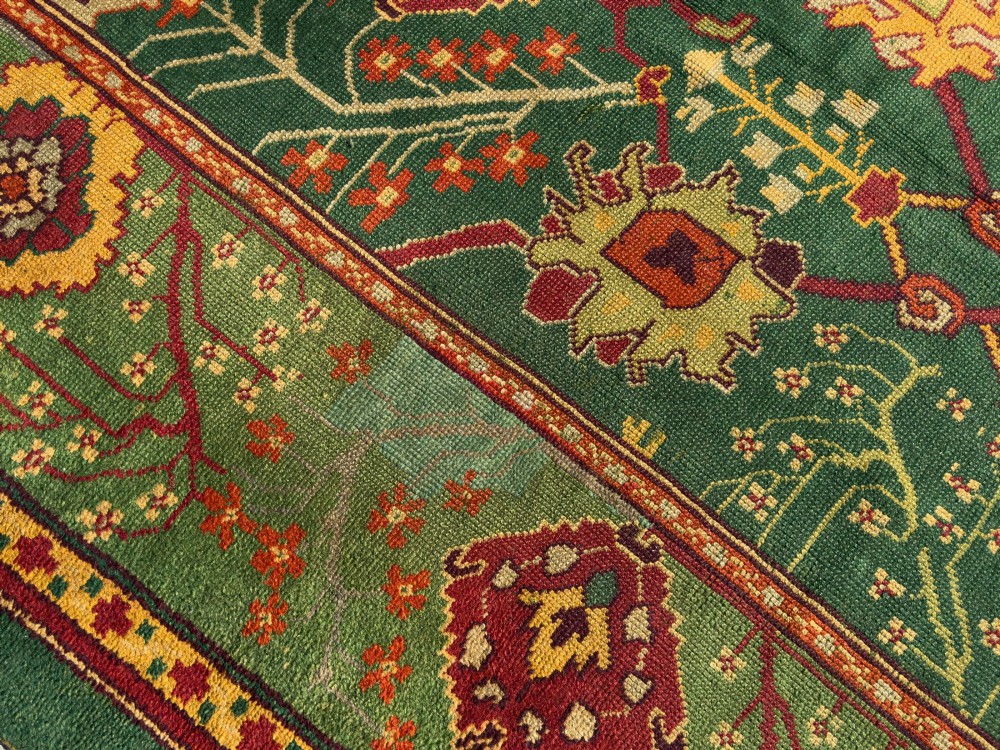 An antique Arts and Crafts hand-knotted wool Donegal carpet featuring a green field filled with stylised red and yellow floral motifs and a decorative geometric border. View V