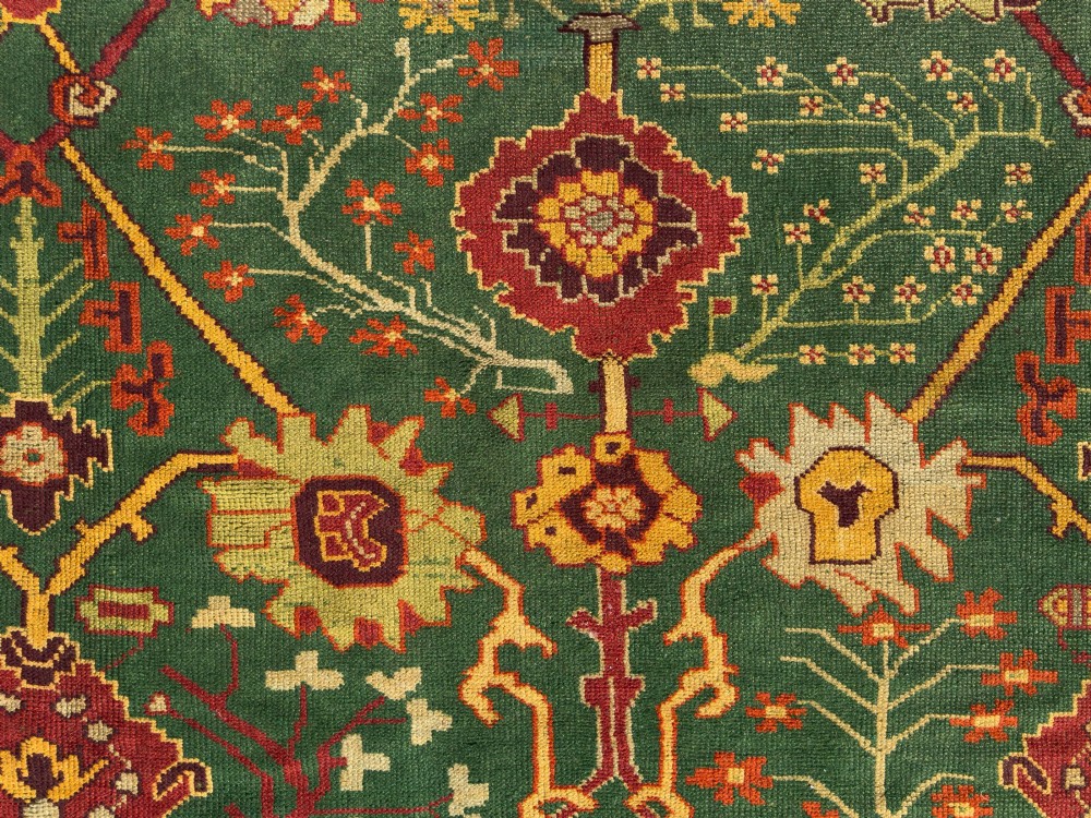 An antique Arts and Crafts hand-knotted wool Donegal carpet featuring a green field filled with stylised red and yellow floral motifs and a decorative geometric border. View VI